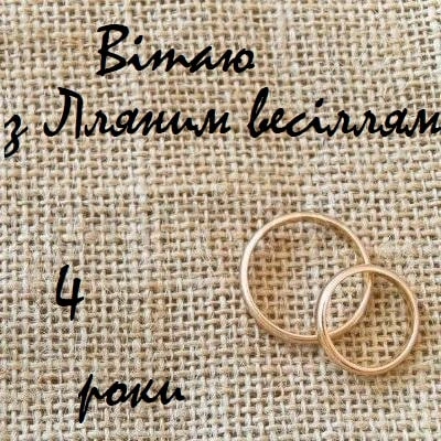Золоті кільця на льняному фоні з привітанням до четвертого весільної річниці.