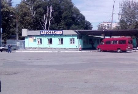 Зображення будівлі автостанції з червоною мікроавтобусом на парковці.
