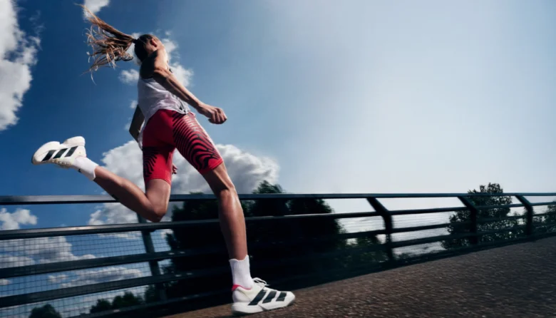 Жінка бігає в одязі Adidas на мосту під синім небом