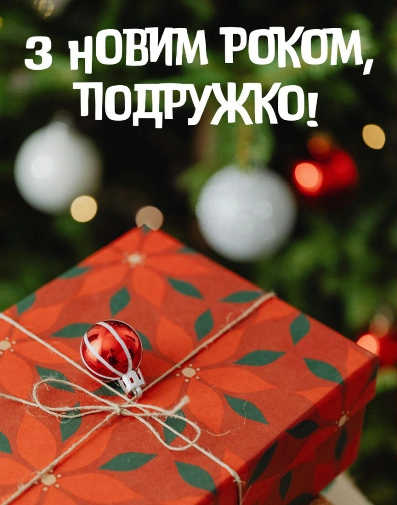 Червона подарункова коробка перед різдвяною ялинкою з привітанням на Новий рік.